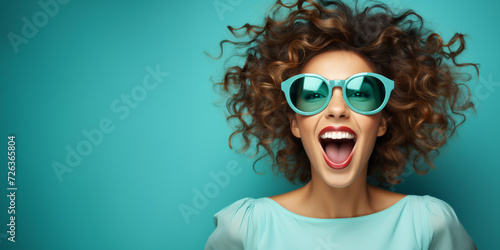 A young woman on a turquoise background with space for text, overjoyed by information or an attractive offer, laughs at the viewer. photo