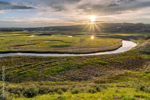 A river meander through a green open meadow with the low sun reflecting off the water at sunset, Trout Creek, Hayden Valley, Yellowstone National Park, Wyoming