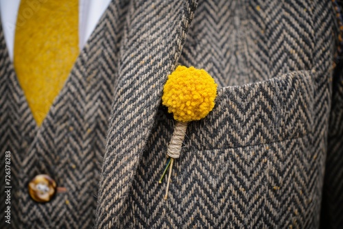 a yellow billy ball boutonniere on a hipsters herringbone vest