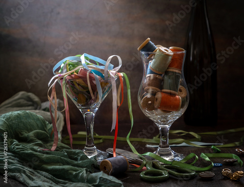Modern still life with spools of multi-colored threads and satin ribbons on a dark background