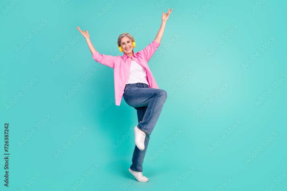 Full size photo of good mood person dressed pink shirt jeans in headphones raising hands up isolated on turquoise color background