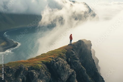Person Overlooking Foggy Mountainous Coastline. A solitary figure in red stands on a cliff, contemplating a misty mountainous coastline bathed in soft light.