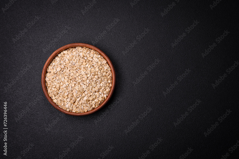Raw oatmeal flakes in a ceramic bowl on a dark concrete background Raw oatmeal flakes in a ceramic bowl on a dark concrete background