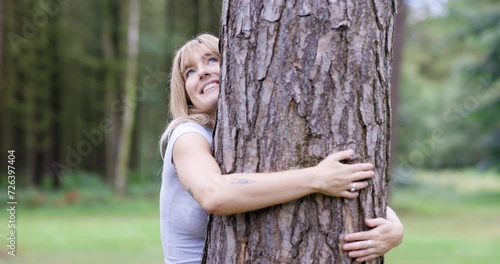 Smiling woman hugging tree in forest photo