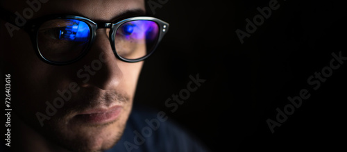 Portrait of a young male programmer wearing computer glasses with blue highlights on a black background with copy space.