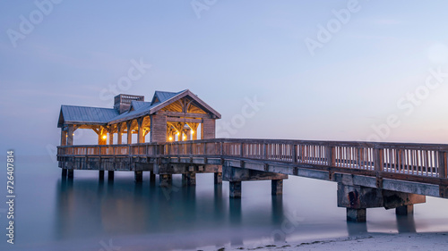Wooden pier, located in Key West, Florida, reaching out into very calm tropical waters at sunset.  There are lights on the structure, as the sky goes dark. © parkerspics