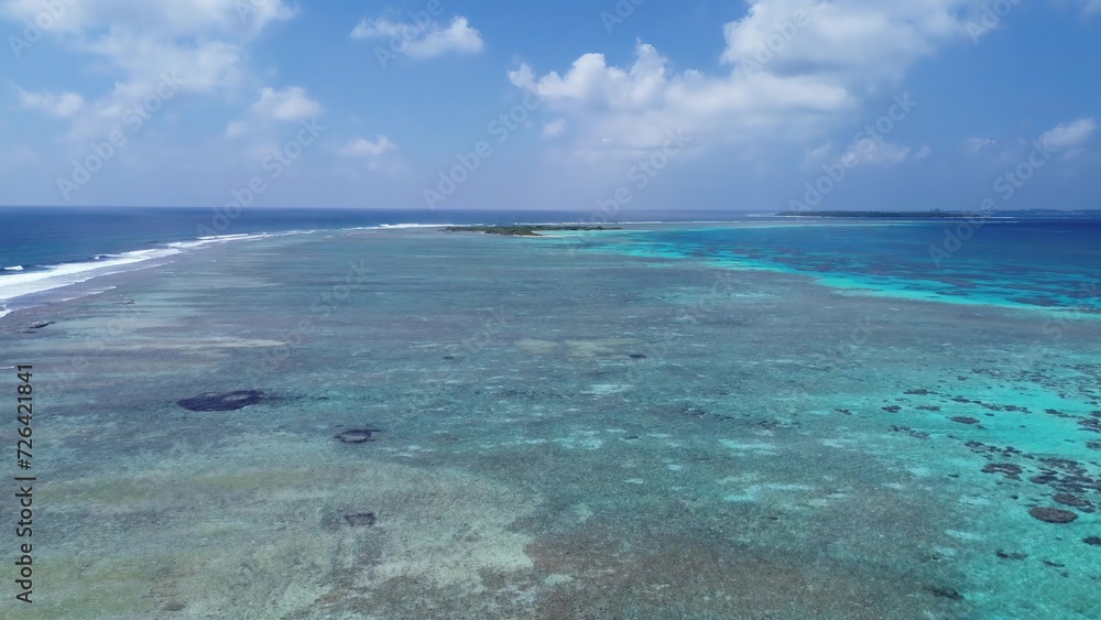 Drone view of paradise islands of the Maldives with coral reefs under the waves of blue the Indian Ocean.