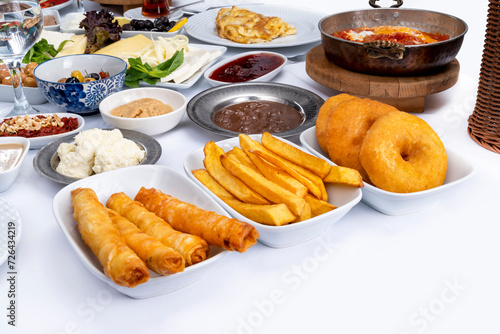 Close up of white breakfast table with mixed various food such as french fries, spring rolls, various jams, honey, cheese, cream, butter, olives, menemen and donuts.