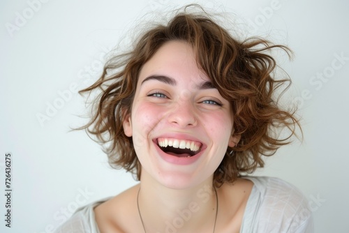 A joyful woman with an infectious smile and vibrant energy radiating from her face, exuding confidence and happiness against a simple wall backdrop in a stunning portrait photograph