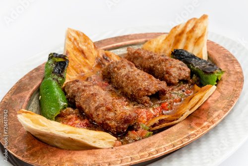 Close up view of lule kebab, the traditional Turkish cuisine shish kebab, with ground meat, pita bread, pepper, and tomato on a copper plate isolated on white background. photo