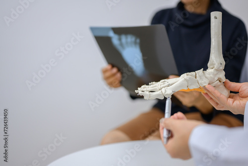 An orthopedic doctor points to a model of ankle and foot bones explaining to a patient a foot bone problem. Health care and spine concept photo