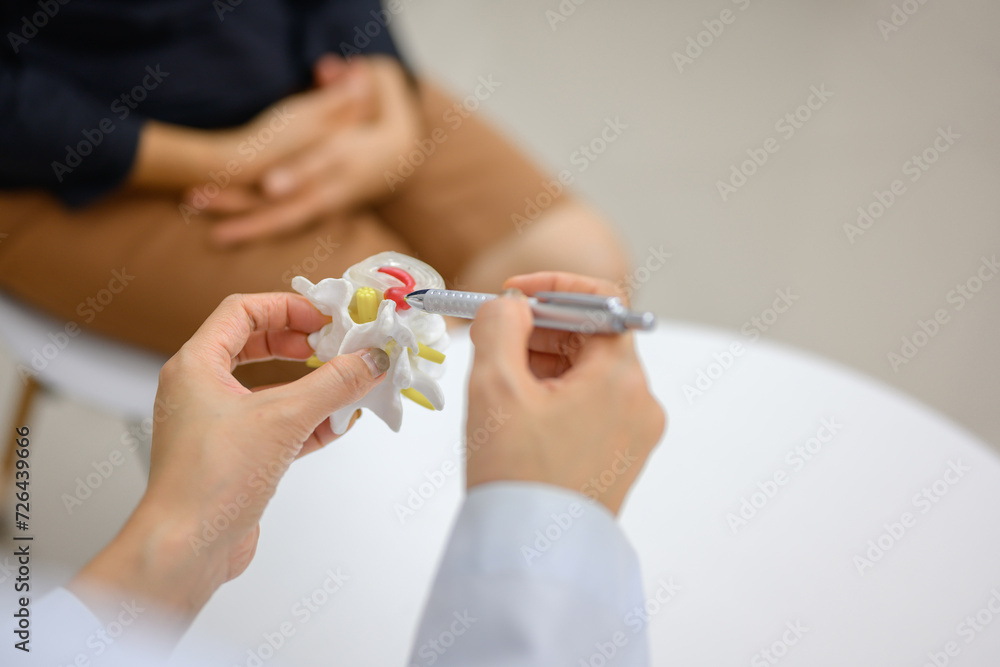 Picture of a close-up of an orthopedic doctor pointing at a spinal model and explaining to a female patient her spinal problems. Health care concept and aging and back pain Picture of a close-up of an orthopedic doctor pointing at a spinal model and explaining to a female patient her spinal problems. Health care concept and aging and back pain