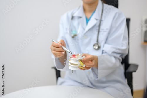 An orthopedic doctor points to a spinal model and explains to the patient her spinal problems. Health care and spine concept