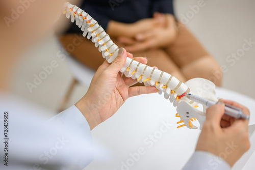 Picture of a close-up of an orthopedic doctor pointing at a spinal model and explaining to a female patient her spinal problems. Health care concept and aging and back pain photo