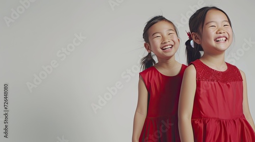 Two pretty asian little girls wearing red dress to celebrate chinesse new year in happy mood isolated on white background. Two siblings with black hair. Chinesse new year celebration concept. photo