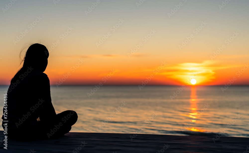 a woman sitting watching a sunset at the sea