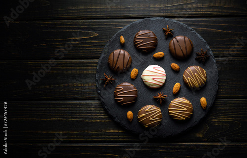 Round cookies with white and dark chocolate on a black serving board with nuts and star anise. Delicious dessert concept on vintage dark kitchen table in restaurant. Advertising space