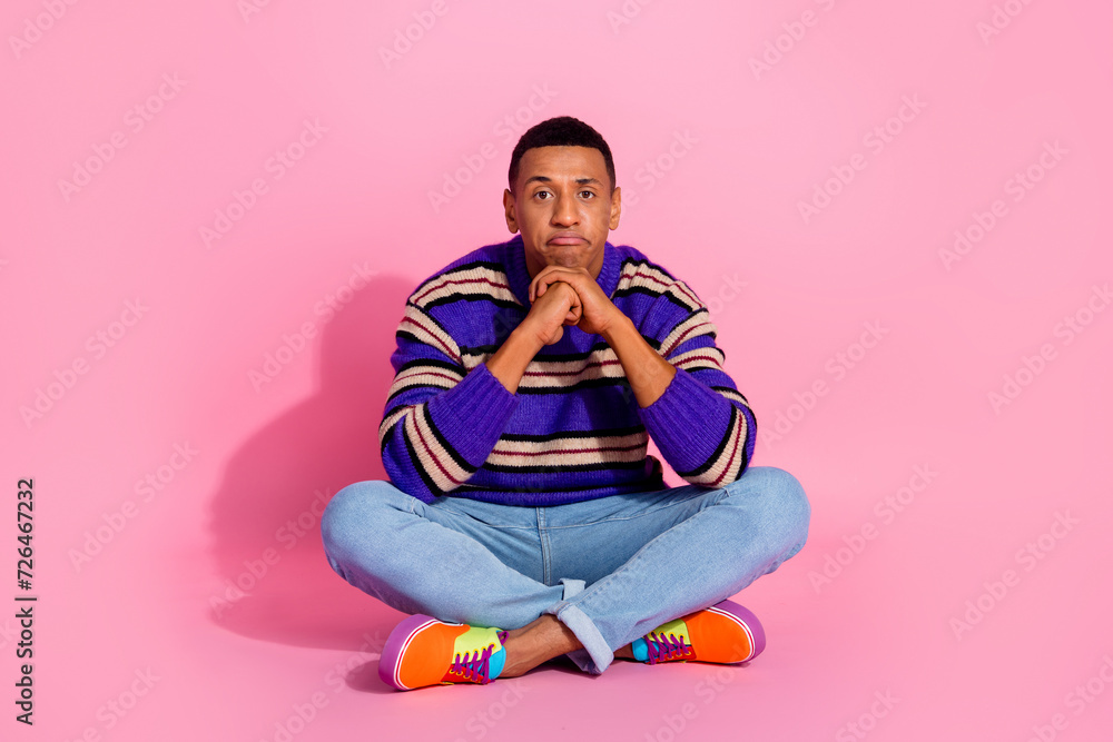 Full length photo of handsome young guy sit floor unhappy face dressed stylish violet striped garment isolated on pink color background Full length photo of handsome young guy sit floor unhappy face dressed stylish violet striped garment isolated on pink color background