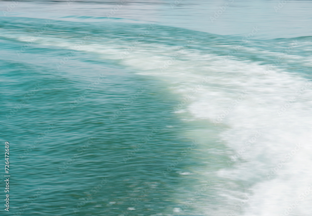 A blurred image of whitewater in a blue-green tropical sea. The soft swells of the water and the curve of the whitewash are balanced against a smooth surface in the upper part of the frame.
