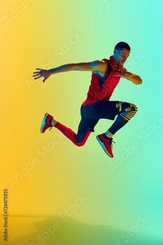 Full-length image of muscular athletic man in sportswear training against gradient blue yellow background in neon light. Concept of active and healthy lifestyle, sport, fitness, endurance