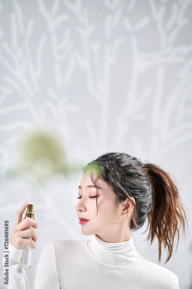 A young, beautiful Asian girl closes her eyes in front of a wall with a shadow of a tree and sprays her face with spray-type cosmetics A young, beautiful Asian girl closes her eyes in front of a wall with a shadow of a tree and sprays her face with spray-type cosmetics