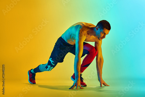 Ready to run. Muscular, sportive young man training shirtless against gradient blue yellow background in neon light. Concept of active and healthy lifestyle, sport, fitness, endurance