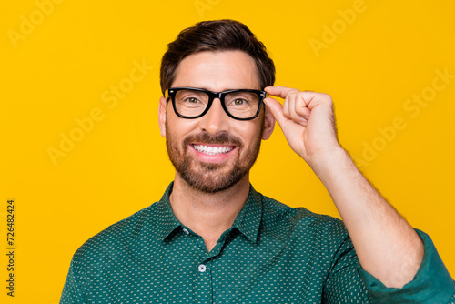 Photo of cheerful clever man with stylish haircut dressed dotted shirt holding eyewear smiling isolated on yellow color background photo