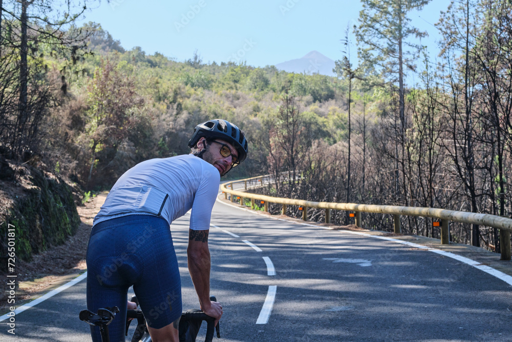 Male cyclist riding on asphalt road through burned forest on Tenerife, Canary Islands, Spain. Sport motivation. Cycling training outdoors in Spain.Cycling adventure. Sportsman training hard on bicycle