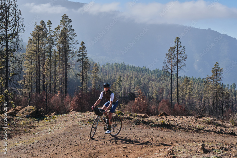 Fototapeta premium Male cyclist riding a gravel bicycle a gravel road through burned forest on Tenerife, Canary Islands, Spain. Sport motivation. Cycling training outdoors in Spain. Cycling adventure .