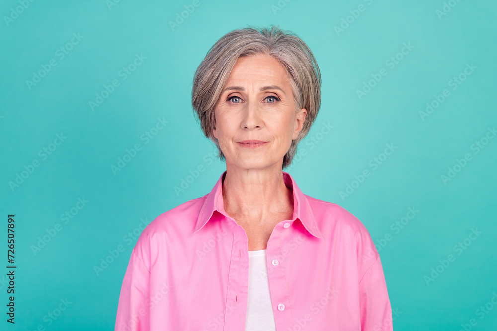 Portrait of old gray haired old business lady in bright pink stylish shirt confident looking forward isolated on cyan color background Portrait of old gray haired old business lady in bright pink stylish shirt confident looking forward isolated on cyan color background
