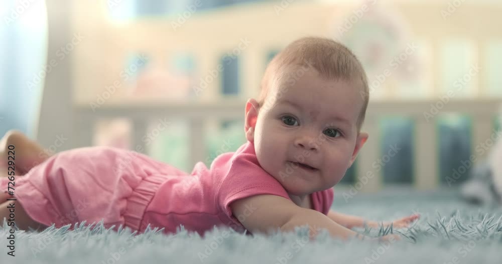 Infant girl lying on crib background in bright room. Little baby smiling, looking at camera. Child dressed in pink clothes lie in bed. Adorable happy toddler at light home. Children happiness indoor Infant girl lying on crib background in bright room. Little baby smiling, looking at camera. Child dressed in pink clothes lie in bed. Adorable happy toddler at light home. Children happiness indoor