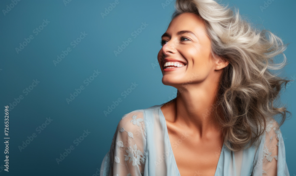 Radiant senior woman with silver hair, beaming with joy, wearing a light blue blouse with lace details, against a soft blue backdrop Radiant senior woman with silver hair, beaming with joy, wearing a light blue blouse with lace details, against a soft blue backdrop