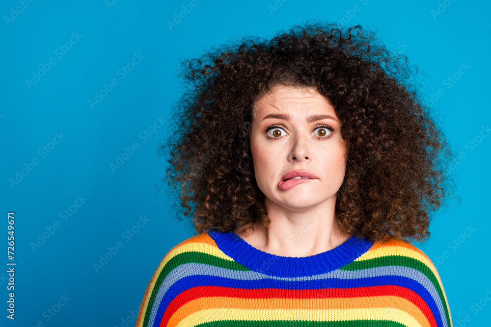 Photo portrait of pretty young girl nervous frightened bite lips wear trendy rainbow print outfit isolated on blue color background Photo portrait of pretty young girl nervous frightened bite lips wear trendy rainbow print outfit isolated on blue color background