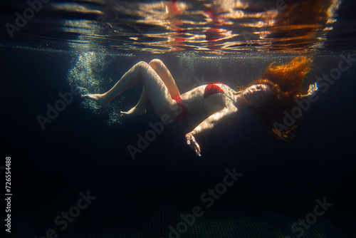 A beautiful sporty girl poses underwater with loose hair against the bright rays of the sun from the surface.
