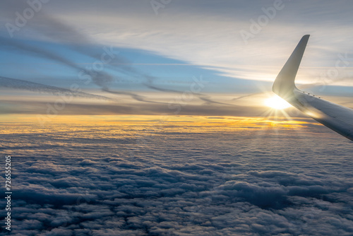 View from an airplane window over a sea of clouds at sunset with the plane wing