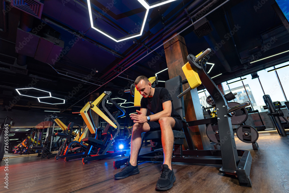 Muscular man sits on bench in the gym and looks at his phone. Muscular man sits on bench in the gym and looks at his phone.