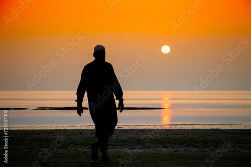 Silhouette of a Muslim man walking on the sea beach during twilight sunset.