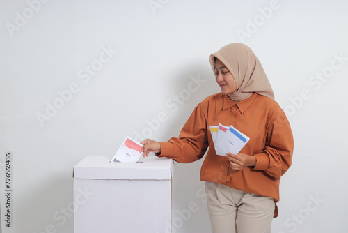 Portrait of Asian hijab woman inserting and putting the voting paper into the ballot box. General elections or Pemilu for the president and government of Indonesia. Isolated image on white background