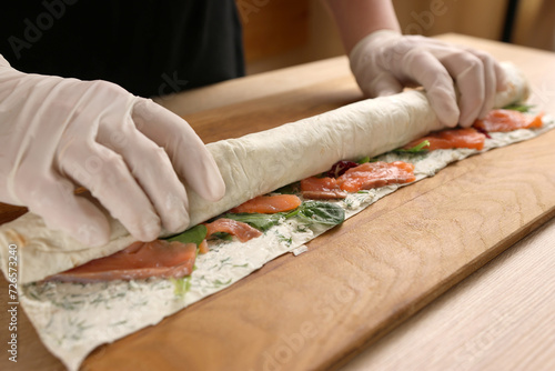 Lavash with filling is wrapped in a roll. Preparation of a roll with cheese, fish and vegetables