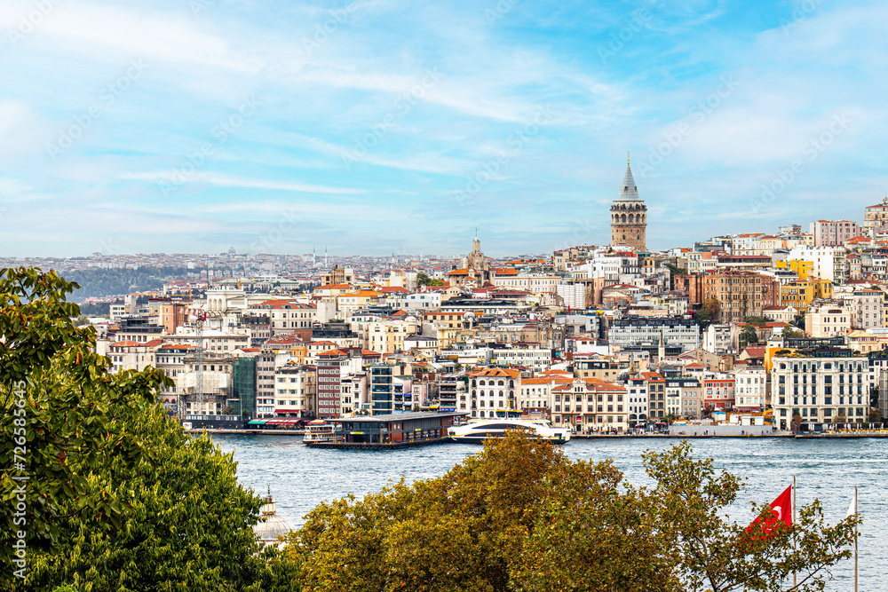 The Galata Tower looms over the dense, colorful buildings of Istanbul's skyline, with the bustling Bosphorus in the foreground, encapsulating the city's vibrant urban life.