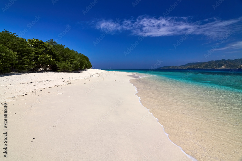 Tropical Asian beach with white sand, turquoise ocean against blue sky with clouds