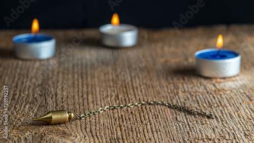 The pendulum on a chain on a background of wood texture with burning candles. Selective focus.