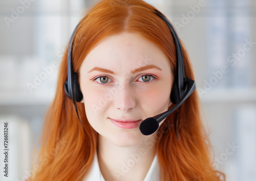 Smiling young woman with red hair works as call center in office with headset and microphone