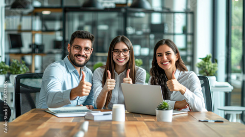 A team of three cheerful business professionals giving thumbs up in a modern office setting, indicating success and approval. © Kowit