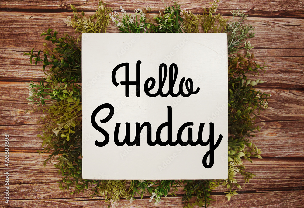 Hello Sunday text message with green leaves decoration on wooden background