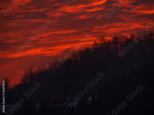 Sunset in the mountains with orange red sky and clouds. Winter Carpathian Mountains view cloudscape. Pine fir tree forest in Carpathians Scenic wood landscape Village in Transcarpathia Ukraine  Europe