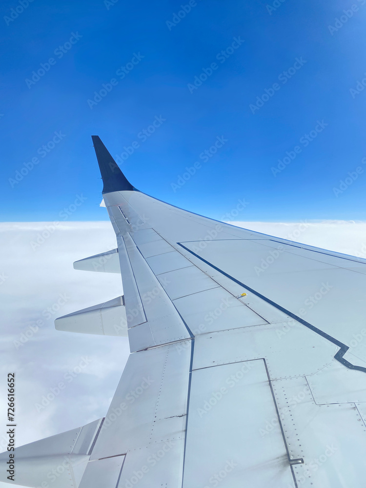 Wing of airplane. View from an aircraft window. Plane's white and blue wing with clouds on a blue sky.