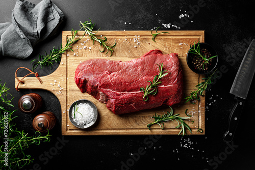 Beef meat entrecote on a cutting board, raw beef meat fillet on black background, top view photo