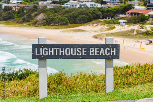 Australian coast, Lighthouse Beach information board with the name of the beach at the entrance to the sandy beach, view from the cliff of the coastal buildings.