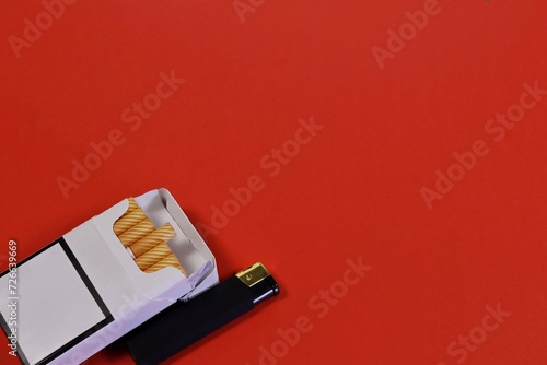 An open pack of cigarettes and a black lighter on a red background. photo